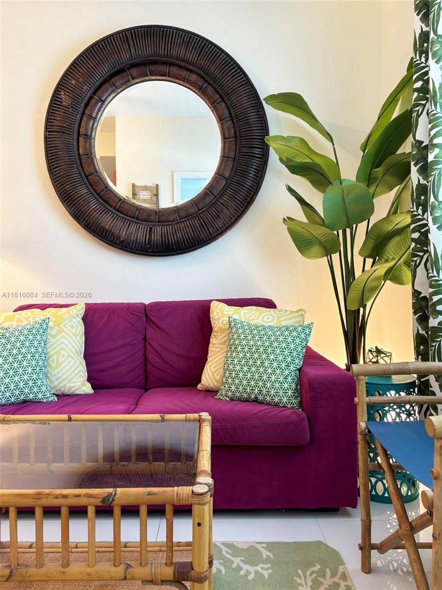 A purple sofa sits in a living room with a round mirror and bamboo furniture — 335 Ocean Dr # 114, Miami Beach FL 33139, MIAMI BEACH, FL