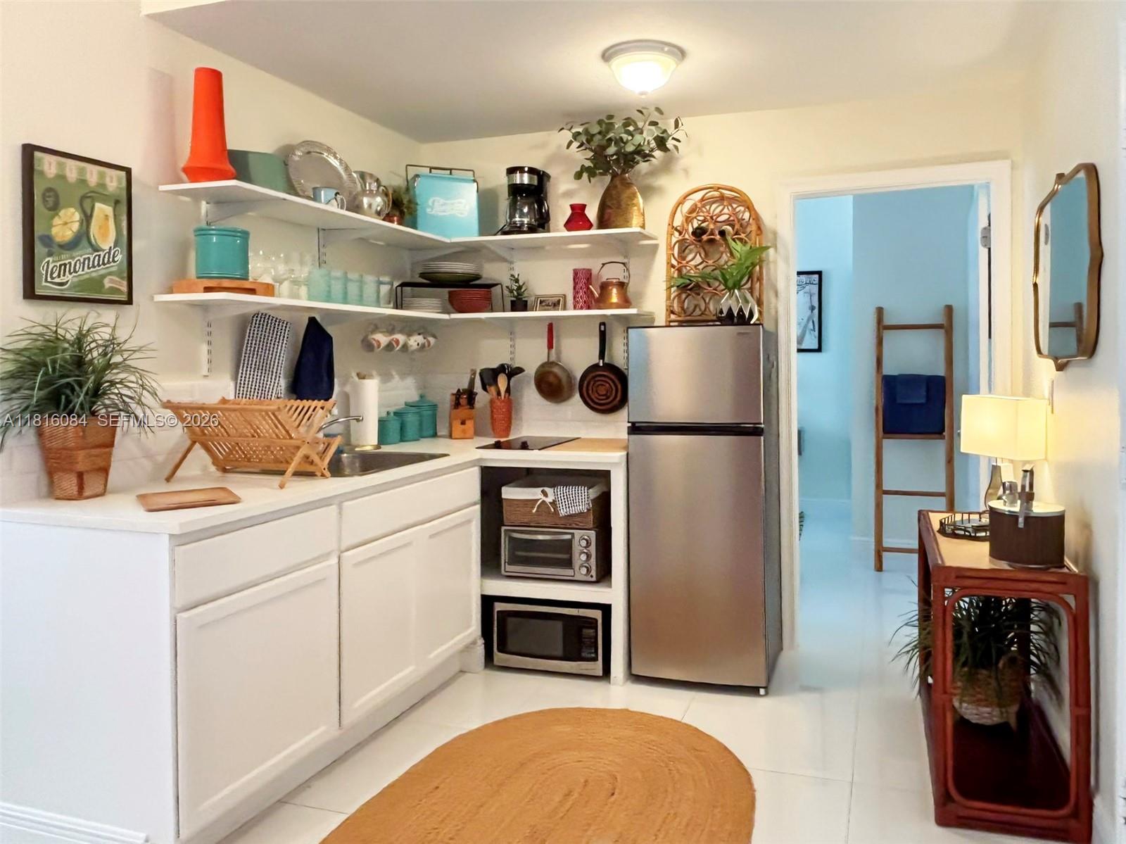 A small kitchen features white cabinets, open shelving, stainless steel appliances, and a jute rug — 335 Ocean Dr # 114, Miami Beach FL 33139, MIAMI BEACH, FL