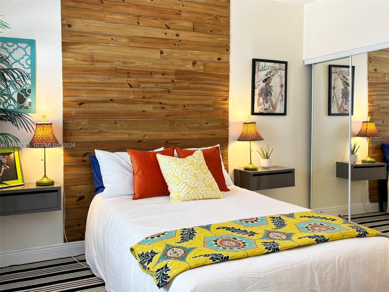 A bedroom features a wood-paneled accent wall, floating nightstands, and a bed with colorful pillows — 335 Ocean Dr # 114, Miami Beach FL 33139, MIAMI BEACH, FL