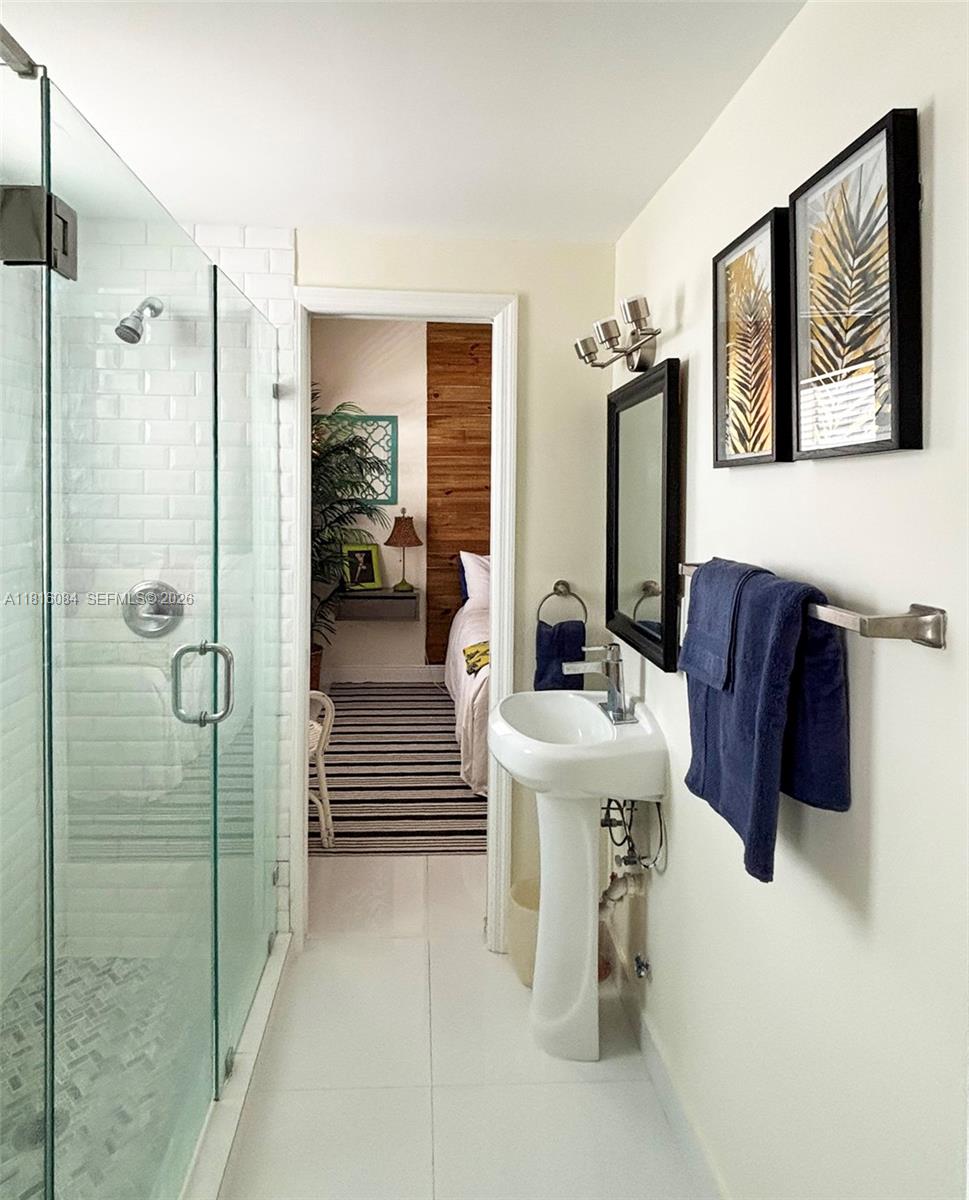 A bathroom features a glass-enclosed shower, a pedestal sink, and a doorway leading to a bedroom — 335 Ocean Dr # 114, Miami Beach FL 33139, MIAMI BEACH, FL