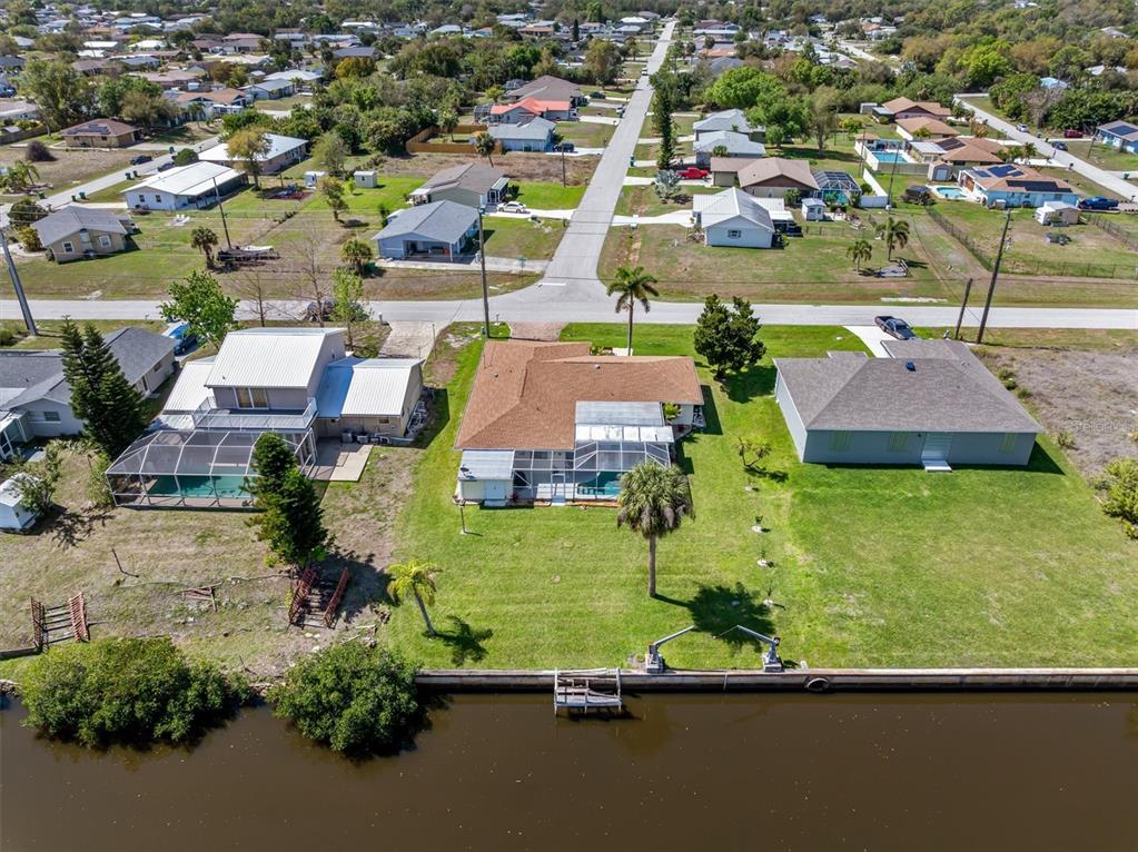 An aerial view shows three waterfront houses with pools and docks along a canal — 2220 BROAD RANCH DRIVE, PORT CHARLOTTE, FL