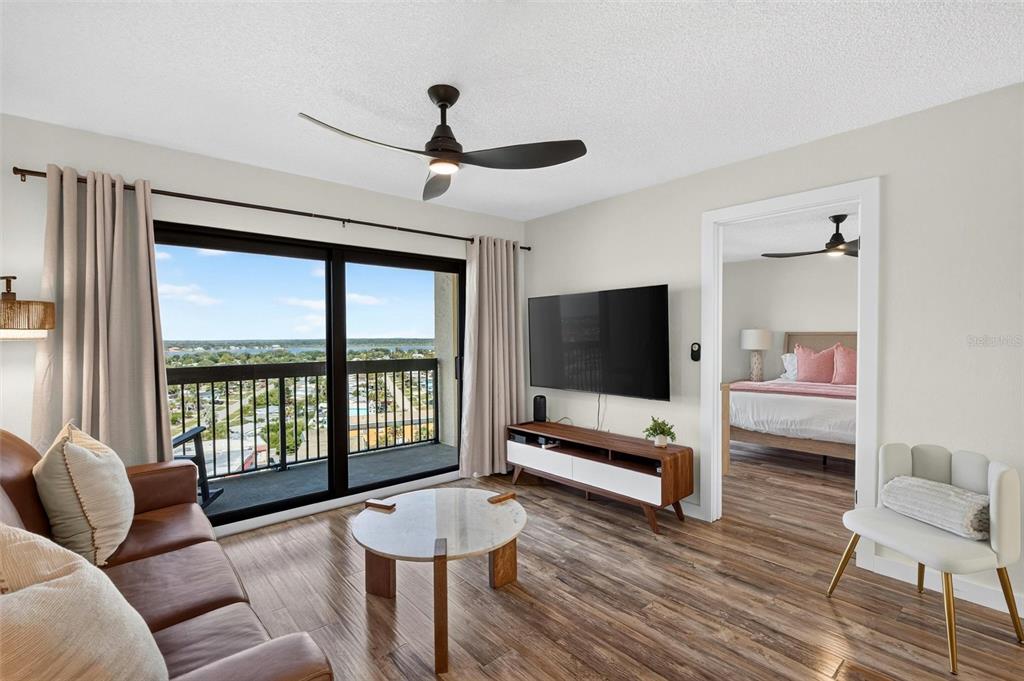 A living room with wood floors, a television, and a balcony overlooking a water view — 1513 OCEAN SHORE BOULEVARD UNIT 10A, ORMOND BEACH, FL
