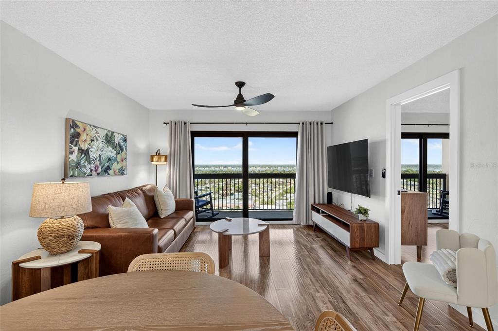 A living room features a brown leather sofa, wood flooring, and a balcony with water views — 1513 OCEAN SHORE BOULEVARD UNIT 10A, ORMOND BEACH, FL
