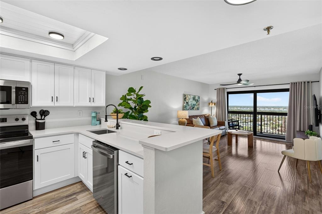 A modern kitchen with white cabinets and stainless steel appliances overlooks a living area — 1513 OCEAN SHORE BOULEVARD UNIT 10A, ORMOND BEACH, FL