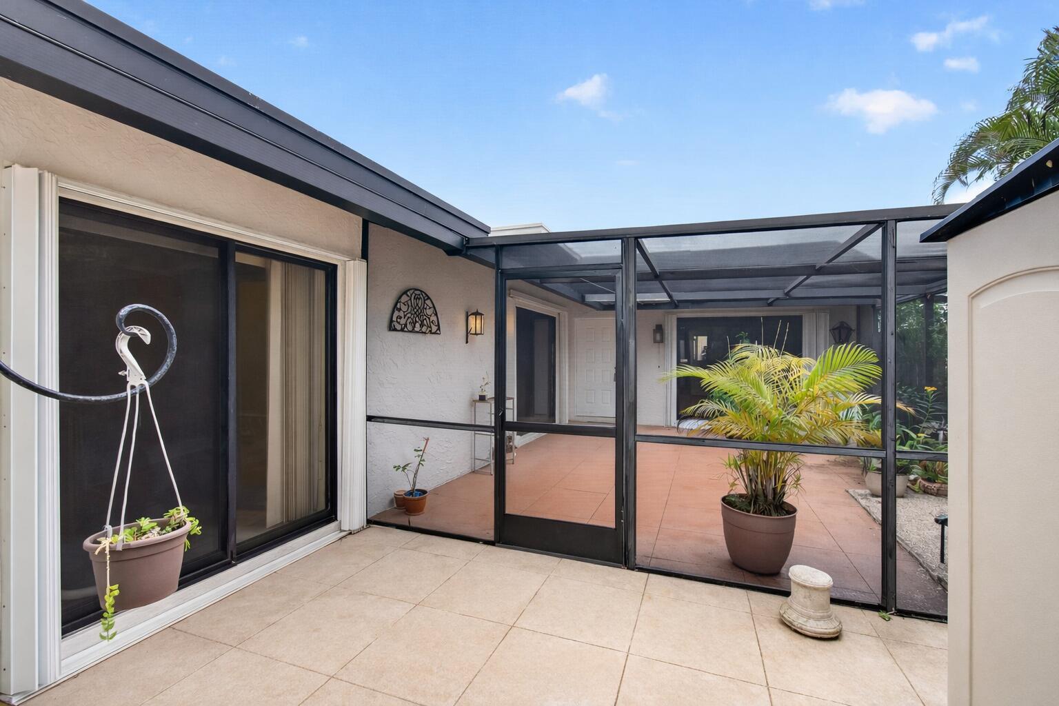 A screened-in patio features tiled flooring, a sliding glass door, and potted plants — 801 NW 30th Avenue # C, Delray Beach FL 33445, DELRAY BEACH, FL