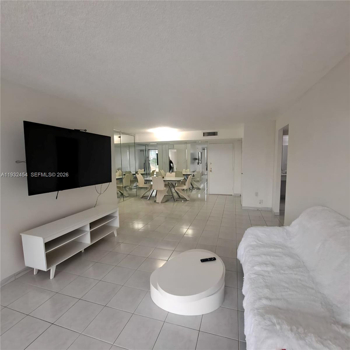 A living room features white tiled floors, a wall-mounted television, and a mirrored dining area — SUNNY ISLES BEACH, FL