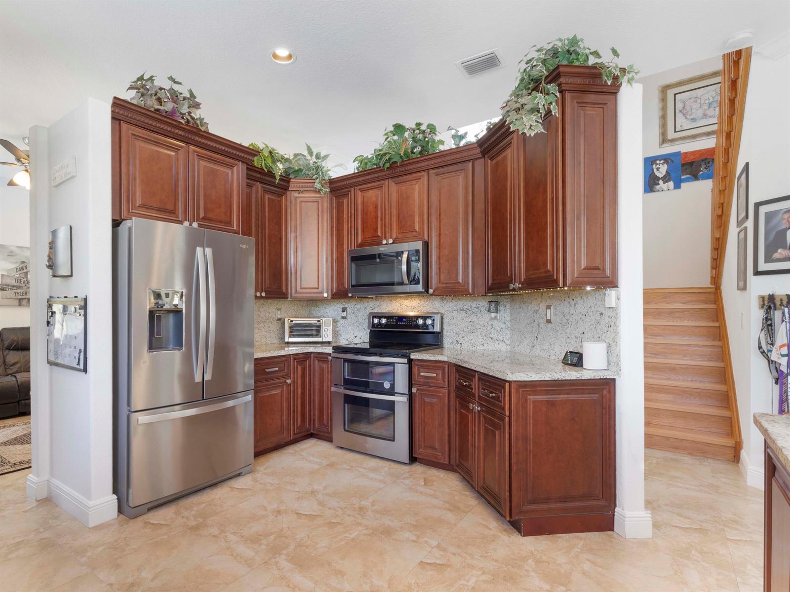 A kitchen features dark wood cabinets, stainless steel appliances, granite countertops, and tile flooring — 6025 Indian Forest Circle, Lake Worth FL 33463, LAKE WORTH, FL