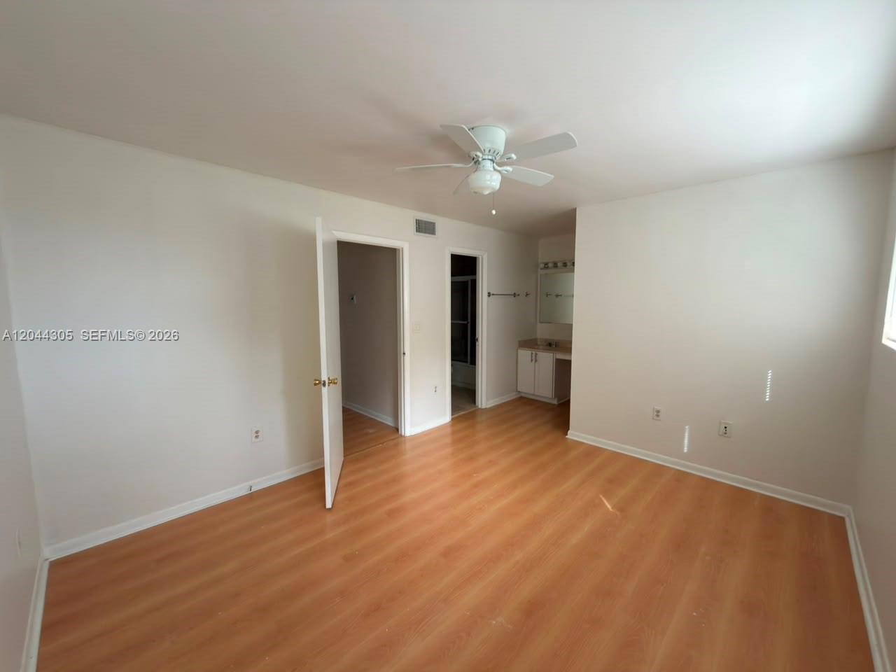 An empty bedroom features light wood-look flooring, a ceiling fan, and an attached bathroom vanity — 862 Crystal Lake Dr, Deerfield Beach FL 33064, DEERFIELD BEACH, FL