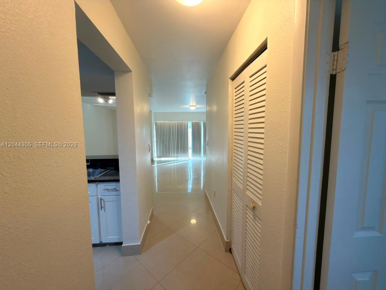 A hallway with tile flooring leads toward a living area with large sliding glass doors — 862 Crystal Lake Dr, Deerfield Beach FL 33064, DEERFIELD BEACH, FL