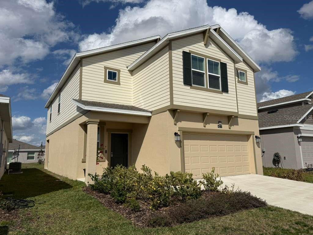 A two-story house with beige stucco and siding, a two-car garage, and a front garden — 4211 TWISTED TWIG BEND, KISSIMMEE, FL