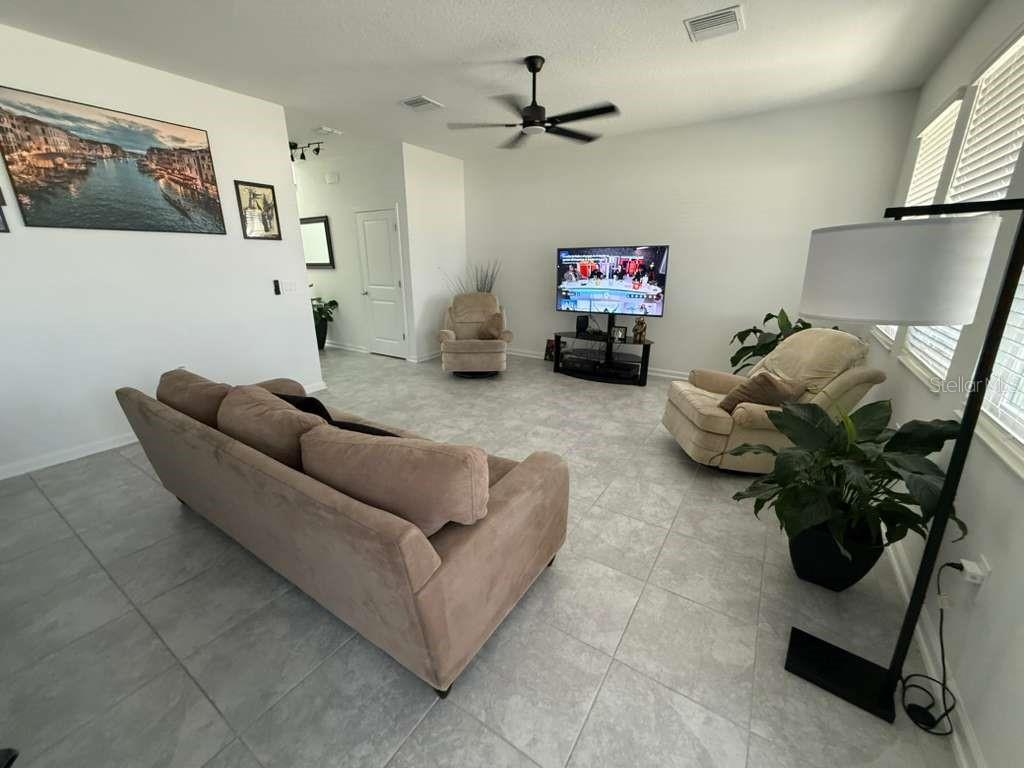 A living room features light tile flooring, a beige sofa, two armchairs, and a television — 4211 TWISTED TWIG BEND, KISSIMMEE, FL