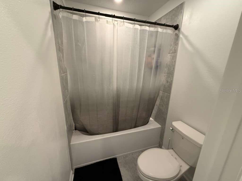 A bathroom features a white toilet and a bathtub with a gray ombre shower curtain — 4211 TWISTED TWIG BEND, KISSIMMEE, FL