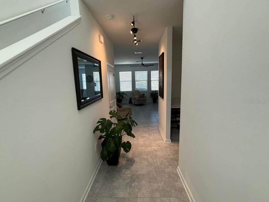A tiled hallway leads from a staircase toward a living area with large windows — 4211 TWISTED TWIG BEND, KISSIMMEE, FL