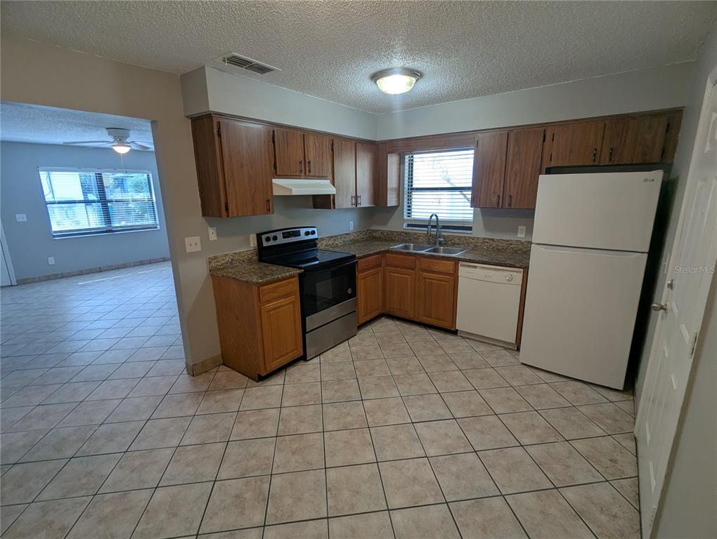 A kitchen features wood cabinets, granite countertops, stainless steel appliances, and tile flooring — 910 SOUTH CENTER STREET UNIT 910, EUSTIS, FL