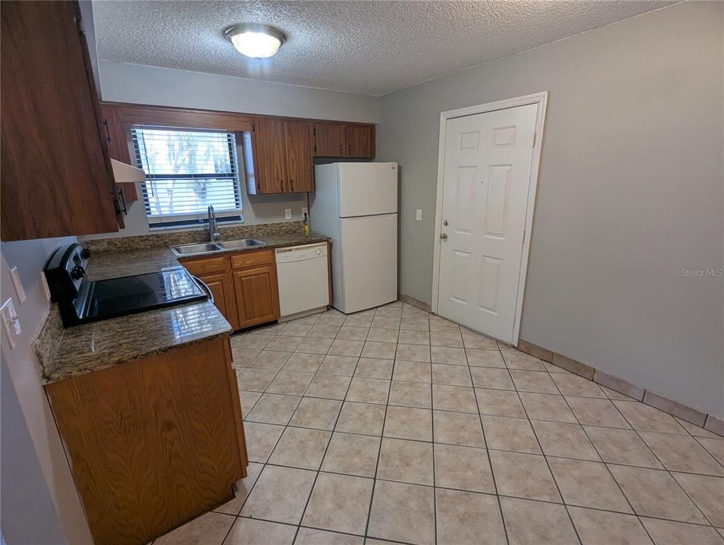 A kitchen with wood cabinets, granite countertops, tile flooring, and a white refrigerator — 910 SOUTH CENTER STREET UNIT 910, EUSTIS, FL