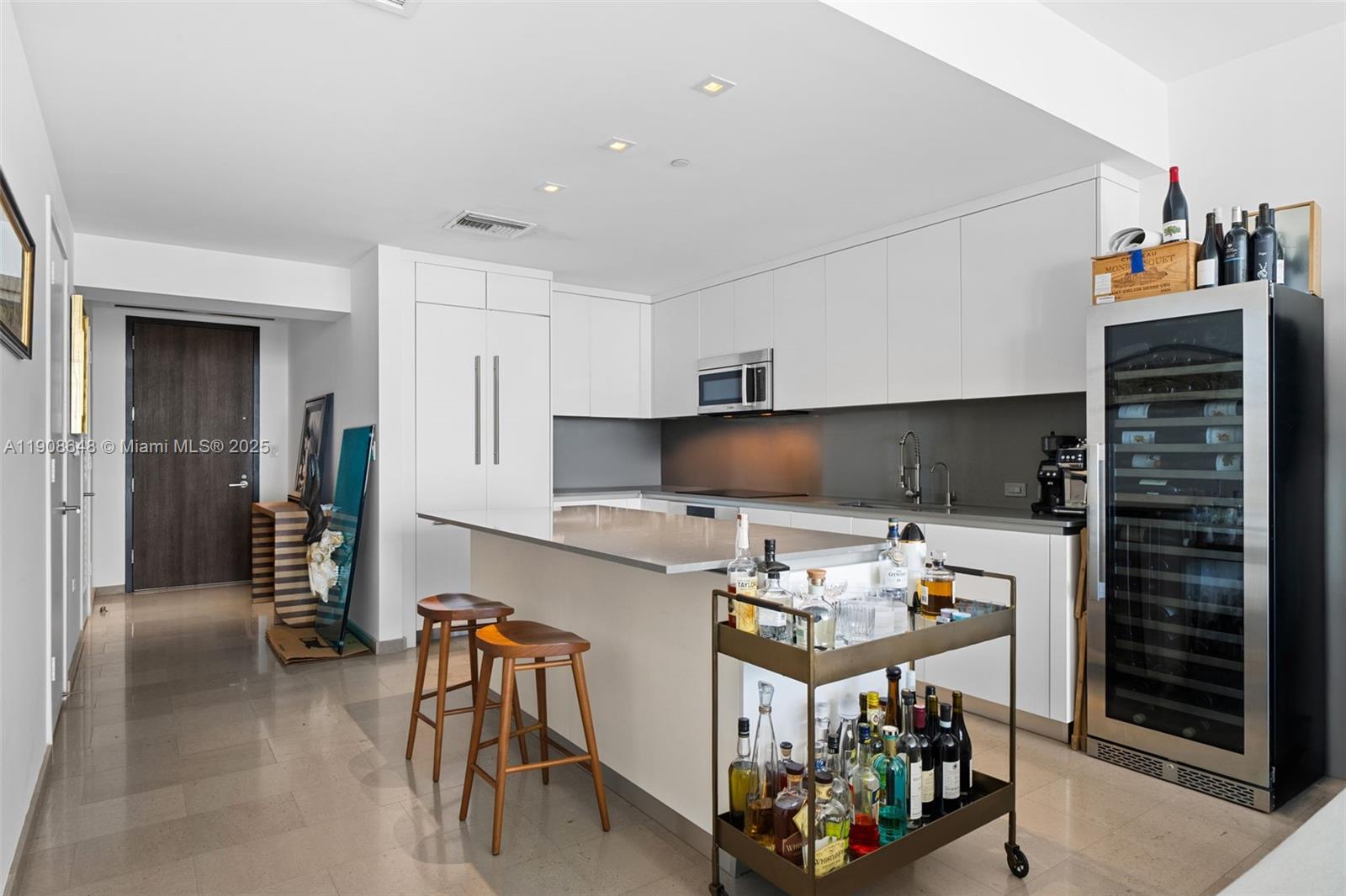 A modern kitchen features white cabinetry, a central island with bar stools, and a wine cooler — 68 SE 6th St # 2505, Miami FL 33131, MIAMI, FL