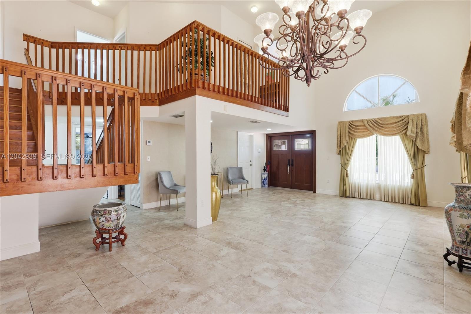 A spacious foyer features tile flooring, a wooden staircase, a chandelier, and a balcony overlook — 15652 SW 91st Ln, Miami FL 33196, MIAMI, FL