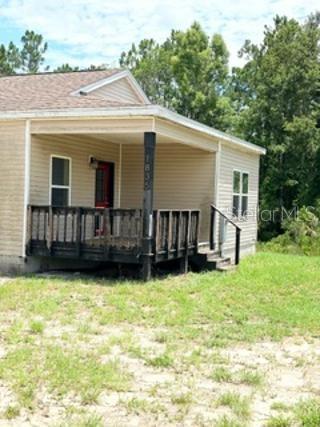 A tan vinyl-sided house features a covered front porch with a dark wooden railing — 1835 SPRINGHEAD DRIVE, DELTONA, FL