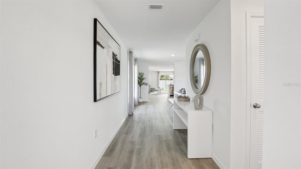 A bright hallway with light wood-look flooring, a white console table, and abstract wall art — 15030 COLTMAN HILL PLACE, WIMAUMA, FL