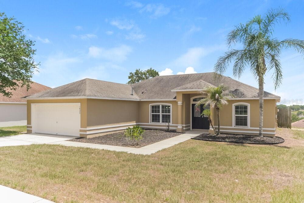 A single-story tan house with a two-car garage, a palm tree, and a front walkway — 1625 NIGHTFALL DRIVE, CLERMONT, FL