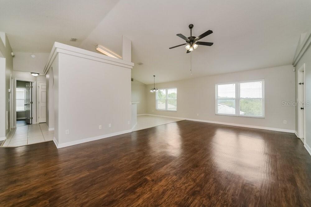 An open-concept living area features dark wood-look flooring, light gray walls, and a ceiling fan — 1625 NIGHTFALL DRIVE, CLERMONT, FL