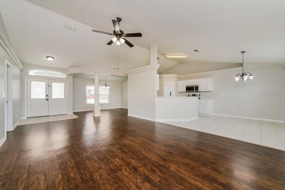 An open-concept living and dining area features dark wood flooring, white cabinets, and vaulted ceilings — 1625 NIGHTFALL DRIVE, CLERMONT, FL