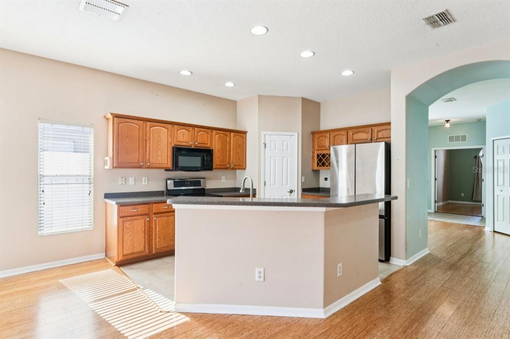 A kitchen with wooden cabinets, stainless steel appliances, and a breakfast bar on hardwood floors — 9314 CREEDMOOR LANE, NEW PORT RICHEY, FL