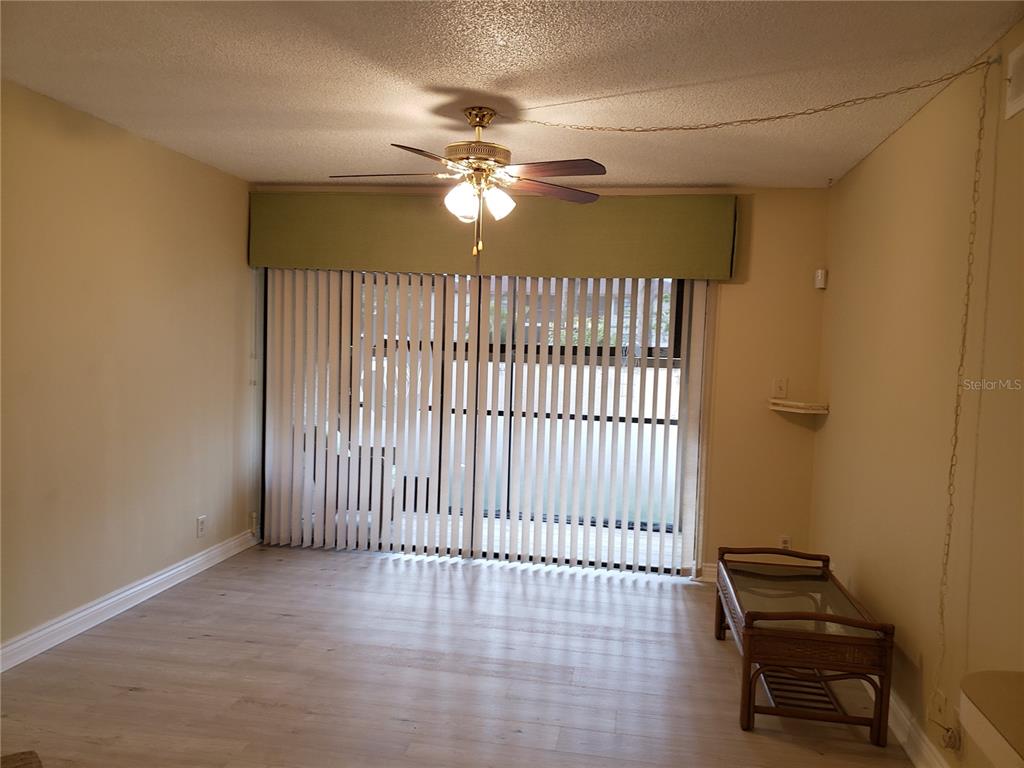 A living room with light wood-look flooring, a ceiling fan, and vertical blinds over sliding doors — 19505 QUESADA UNIT OO103, PORT CHARLOTTE, FL
