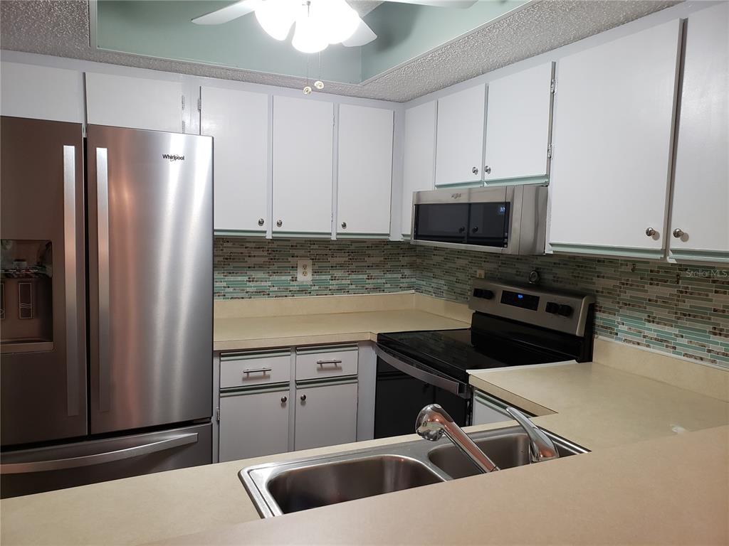 A kitchen features white cabinets, stainless steel appliances, a tiled backsplash, and a double sink — 19505 QUESADA UNIT OO103, PORT CHARLOTTE, FL