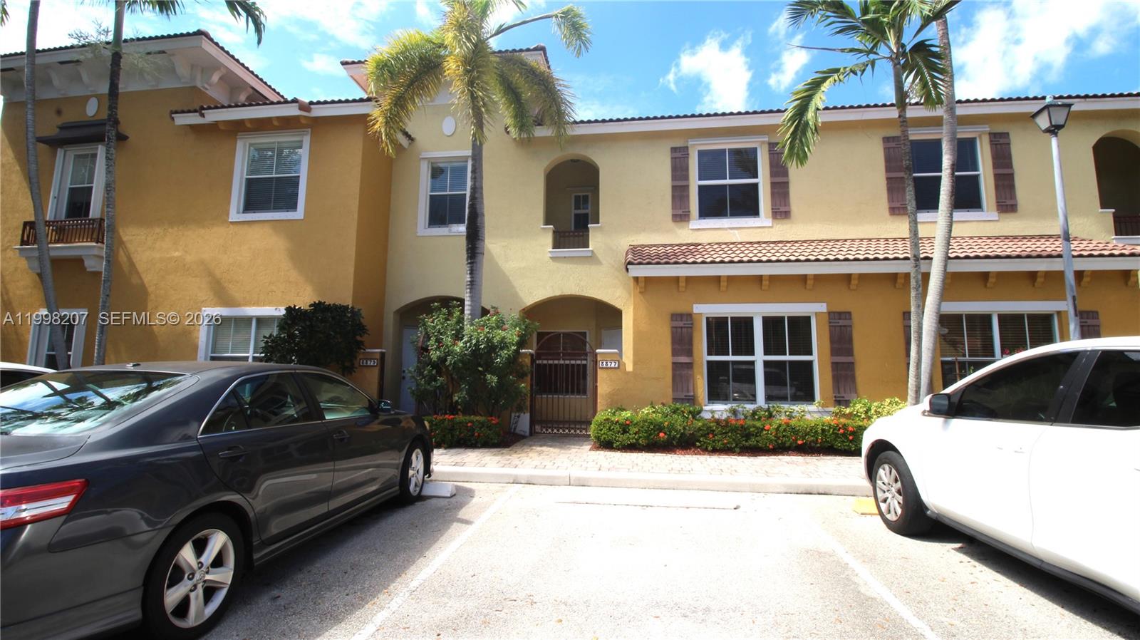 A two-story yellow stucco townhouse features a gated entryway, arched balcony, and brown shutters — 3377 Merrick Ln # 707, Margate FL 33063, MARGATE, FL