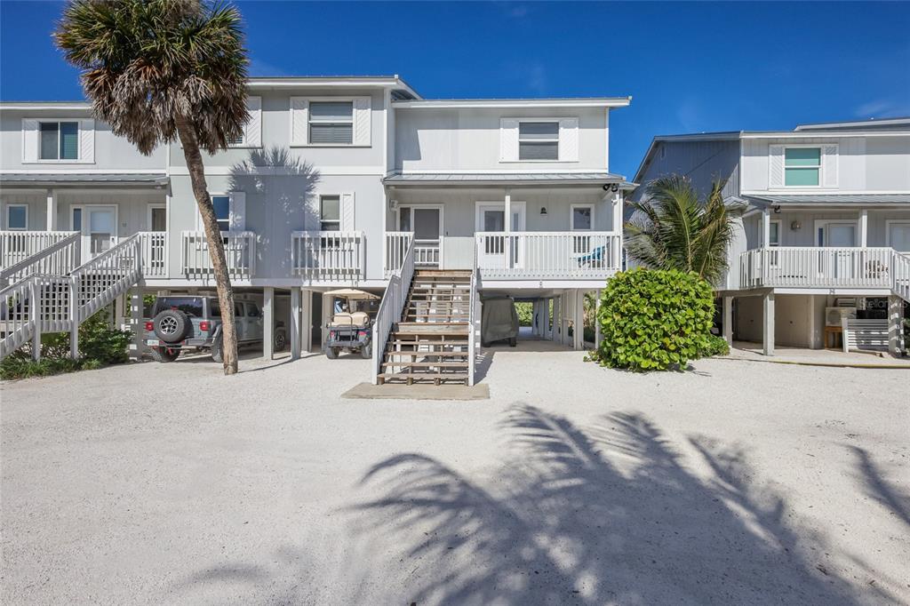 An exterior view of elevated beach houses with white siding, wooden stairs, and sandy ground — 420 GULF BOULEVARD UNIT 9, BOCA GRANDE, FL