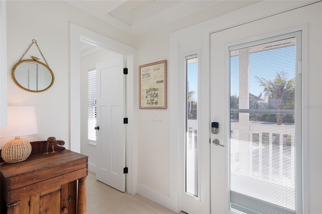 A bright entryway features a wooden cabinet, a round mirror, and a glass-paneled front door — 420 GULF BOULEVARD UNIT 9, BOCA GRANDE, FL