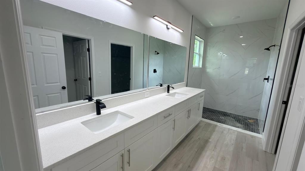 A modern bathroom features a double vanity with white cabinets, quartz countertops, and a shower — 2693 JEANNIN DRIVE, NORTH PORT, FL