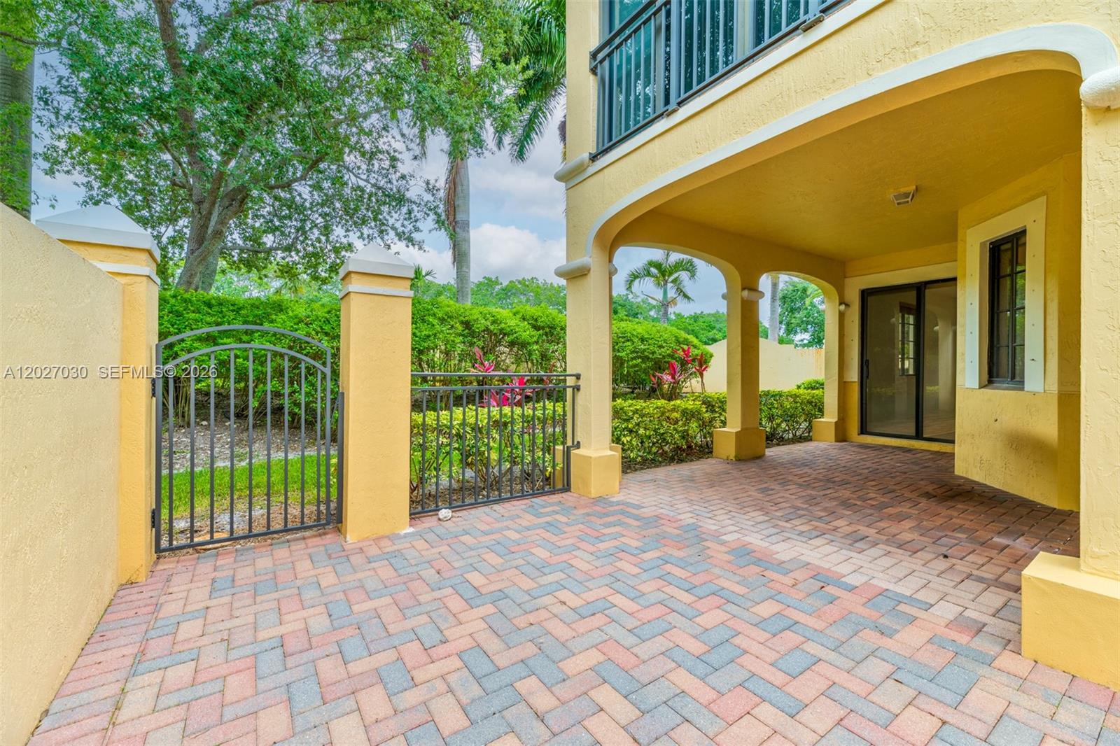 A paved patio features a metal gate, yellow stucco columns, and a sliding glass door — 1695 Passion Vine Cir # 1, Weston FL 33326, WESTON, FL