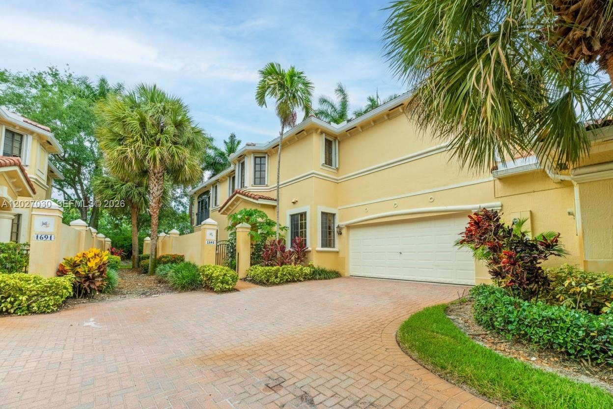 A two-story yellow stucco townhouse features a paved driveway and an attached two-car garage — 1695 Passion Vine Cir # 1, Weston FL 33326, WESTON, FL