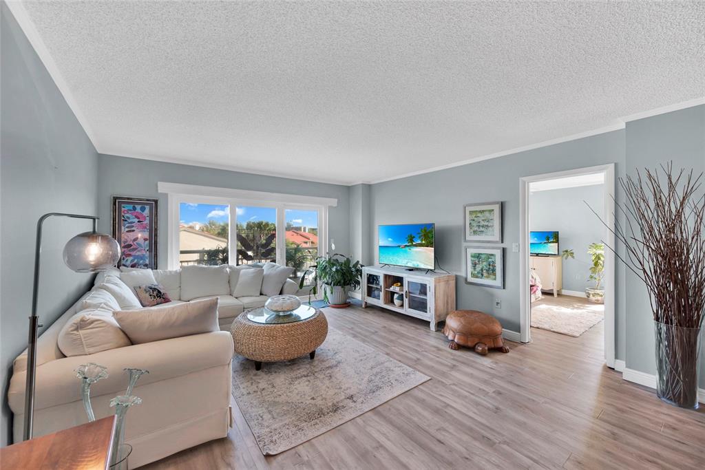 A living room features a white sectional sofa, a round coffee table, and wood-look flooring — 4900 BRITTANY DRIVE S UNIT 301, ST PETERSBURG, FL