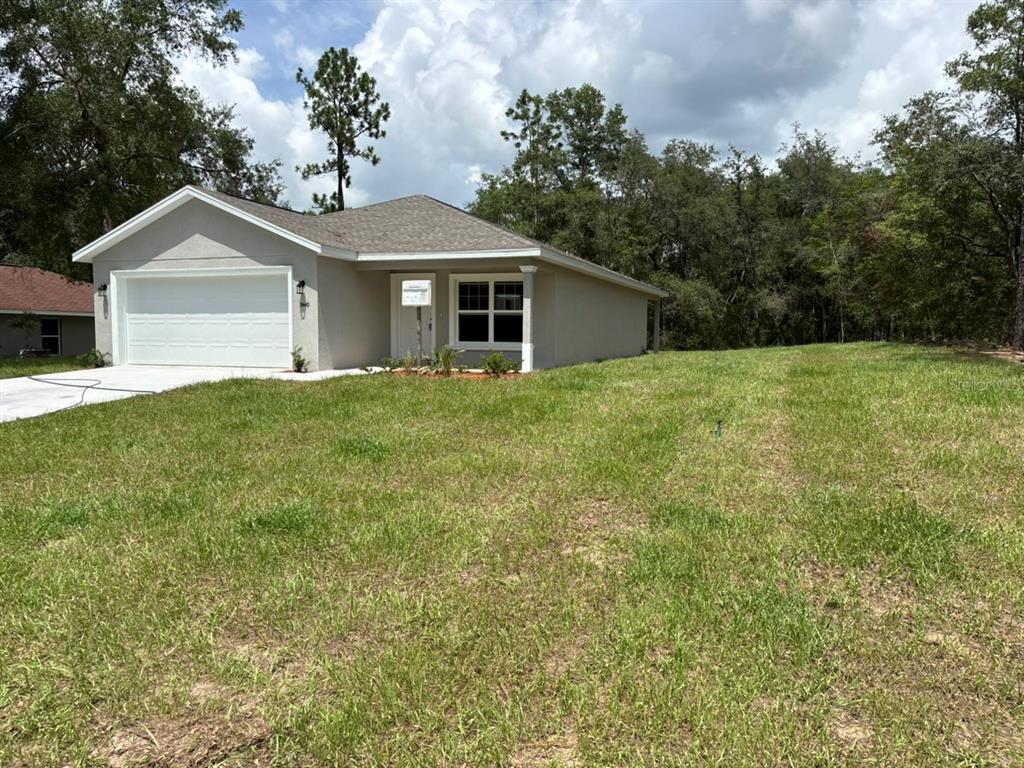 A single-story house with a two-car garage sits on a grassy lot near trees — 9449 N CORTLANDT DRIVE, DUNNELLON, FL