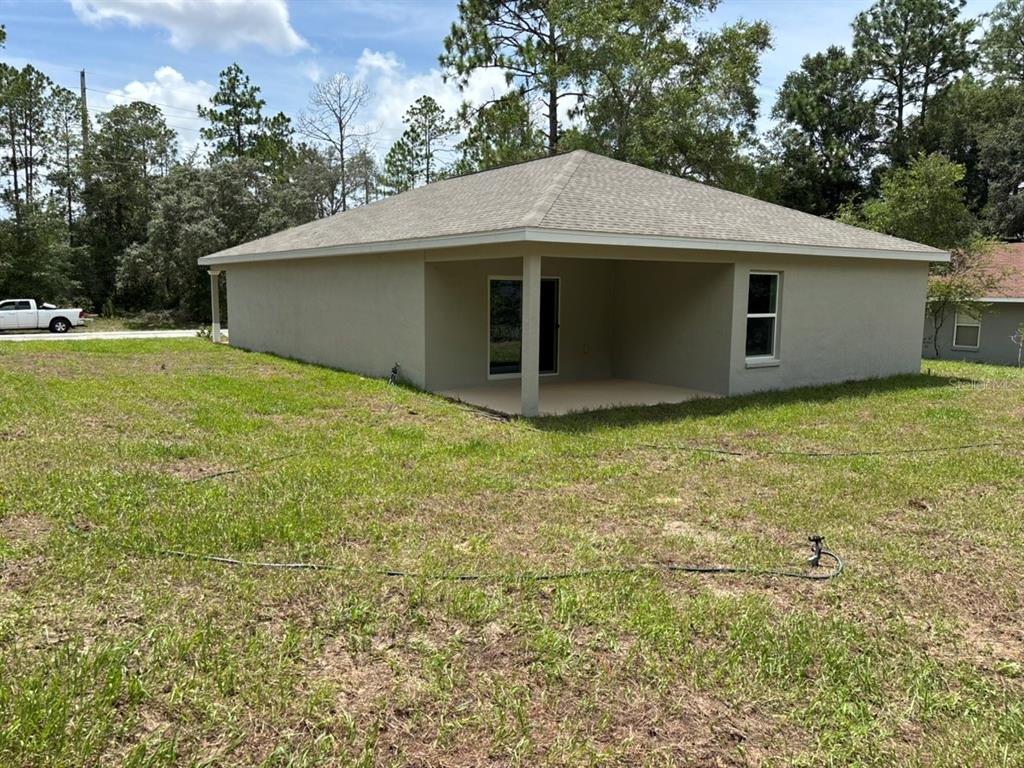 The exterior of a tan, single-story house features a covered patio and a grassy yard — 9449 N CORTLANDT DRIVE, DUNNELLON, FL