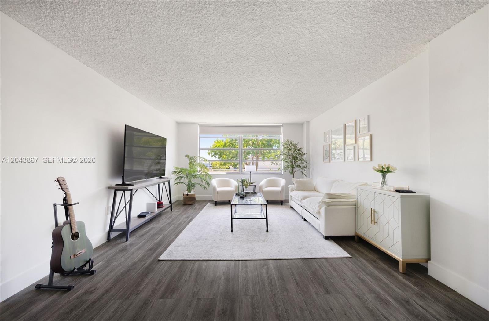A living room features white walls, dark wood-look flooring, a white sofa, and a television — 150 SE 25th Rd # 2J, Miami FL 33129, MIAMI, FL