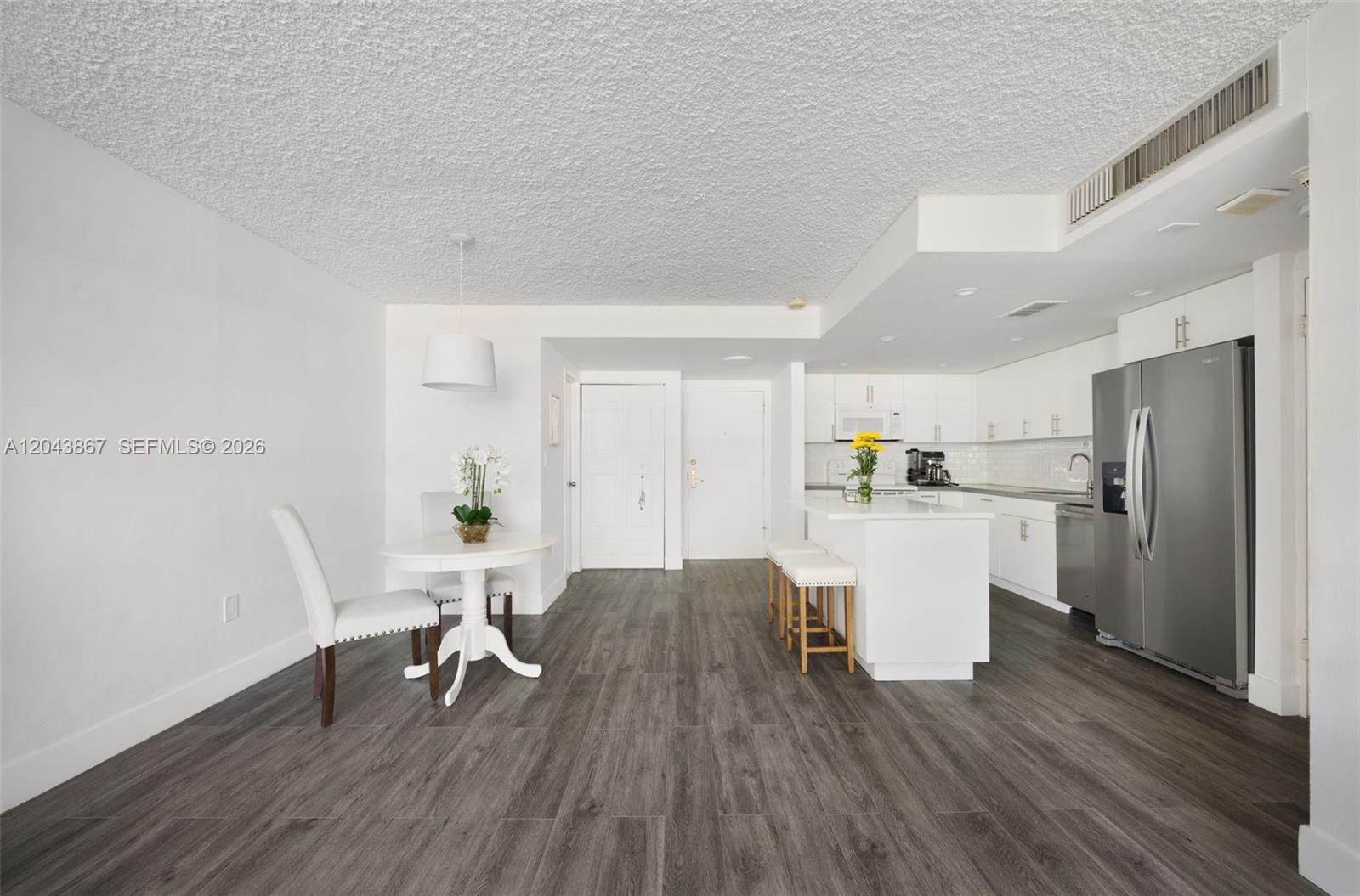 A bright, open-concept kitchen and dining area features white cabinetry, stainless appliances, and wood-look flooring — 150 SE 25th Rd # 2J, Miami FL 33129, MIAMI, FL