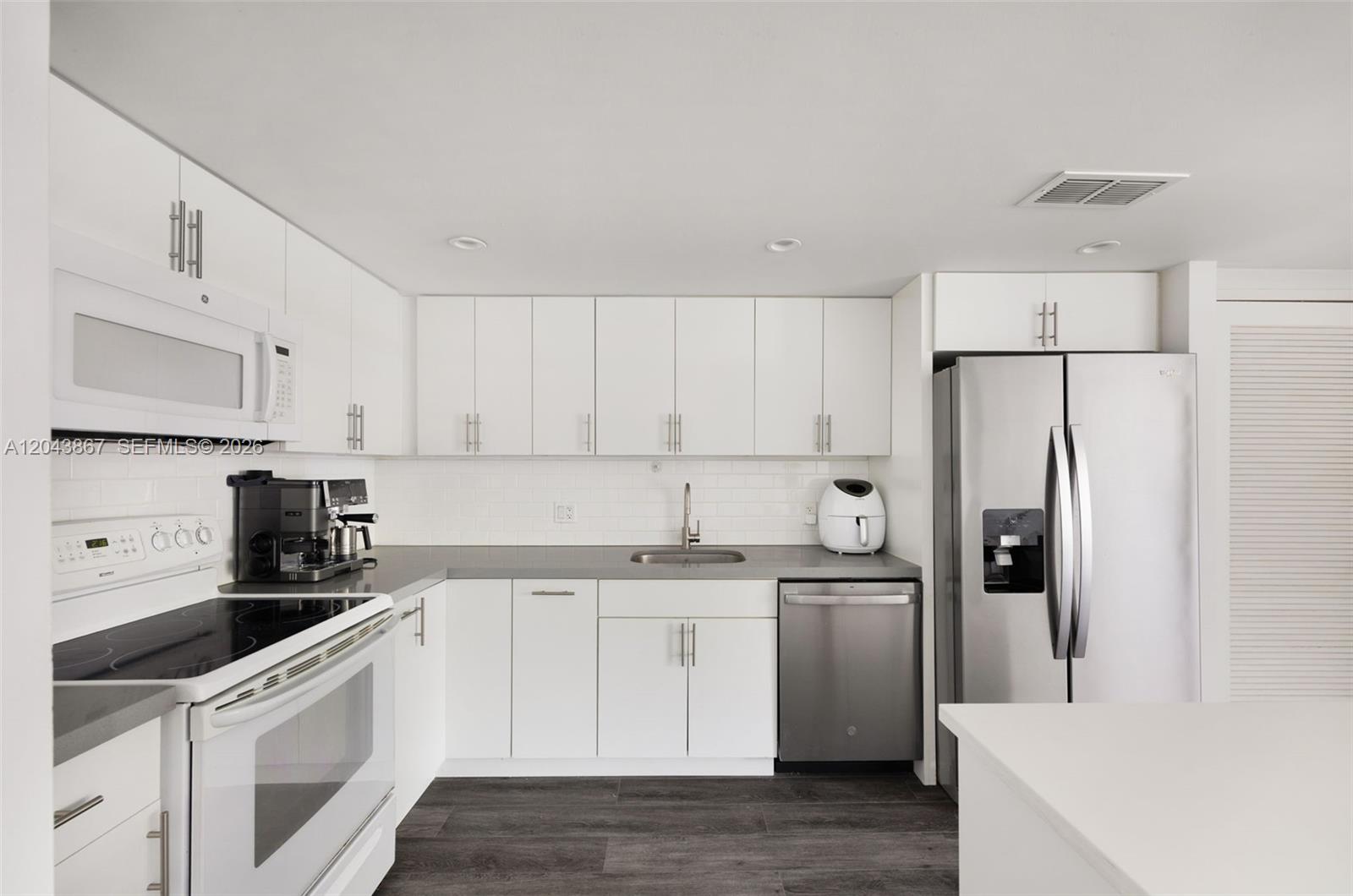 A kitchen features white cabinetry, stainless steel appliances, gray countertops, and dark wood-look flooring — 150 SE 25th Rd # 2J, Miami FL 33129, MIAMI, FL