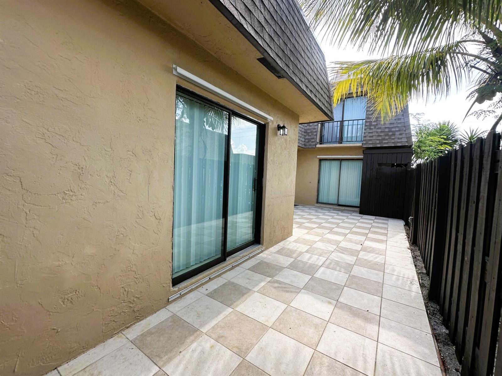 A tan stucco exterior features a sliding glass door opening onto a tiled patio area — 303 Waterview Drive, Palm Springs FL 33461, PALM SPRINGS, FL