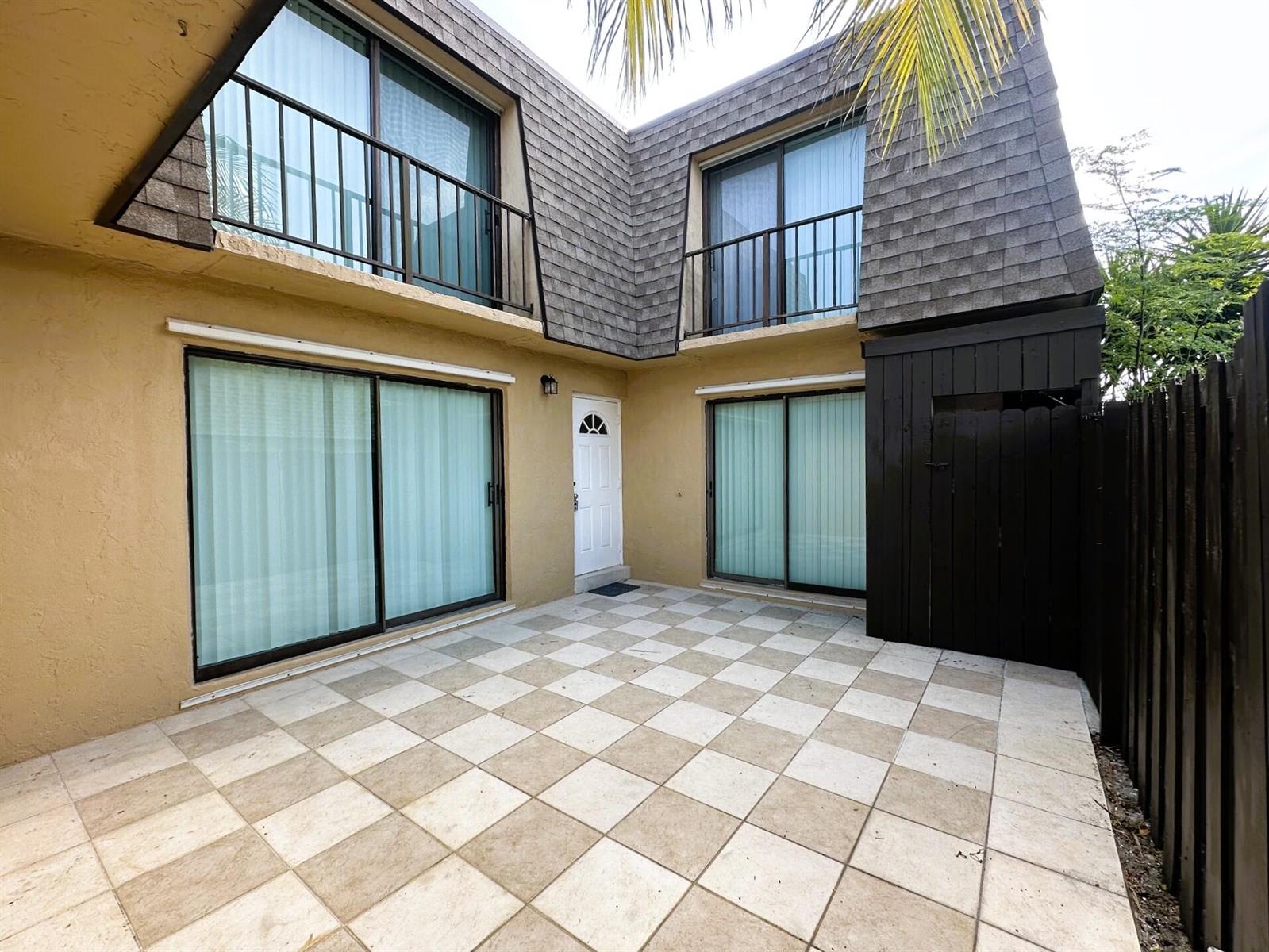 A paved patio sits in front of a two-story building with sliding glass doors and balconies — 303 Waterview Drive, Palm Springs FL 33461, PALM SPRINGS, FL