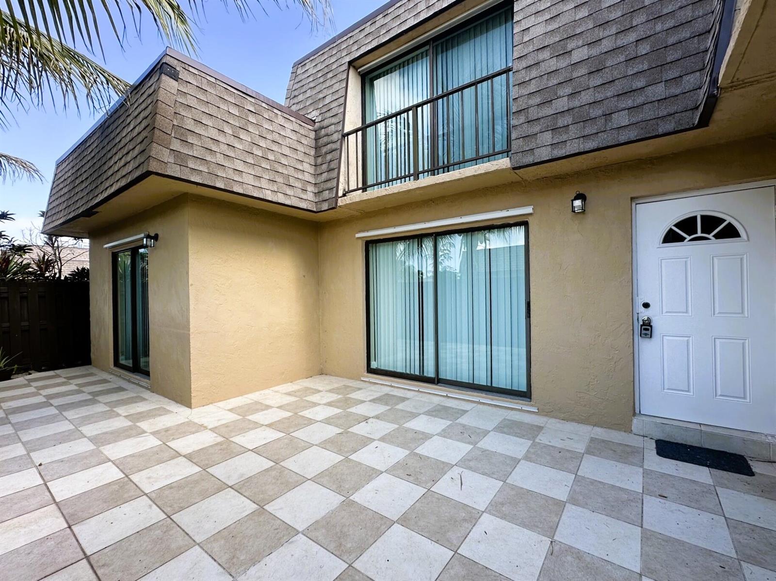 A two-story building exterior features a checkered patio, sliding glass doors, and a white door — 303 Waterview Drive, Palm Springs FL 33461, PALM SPRINGS, FL