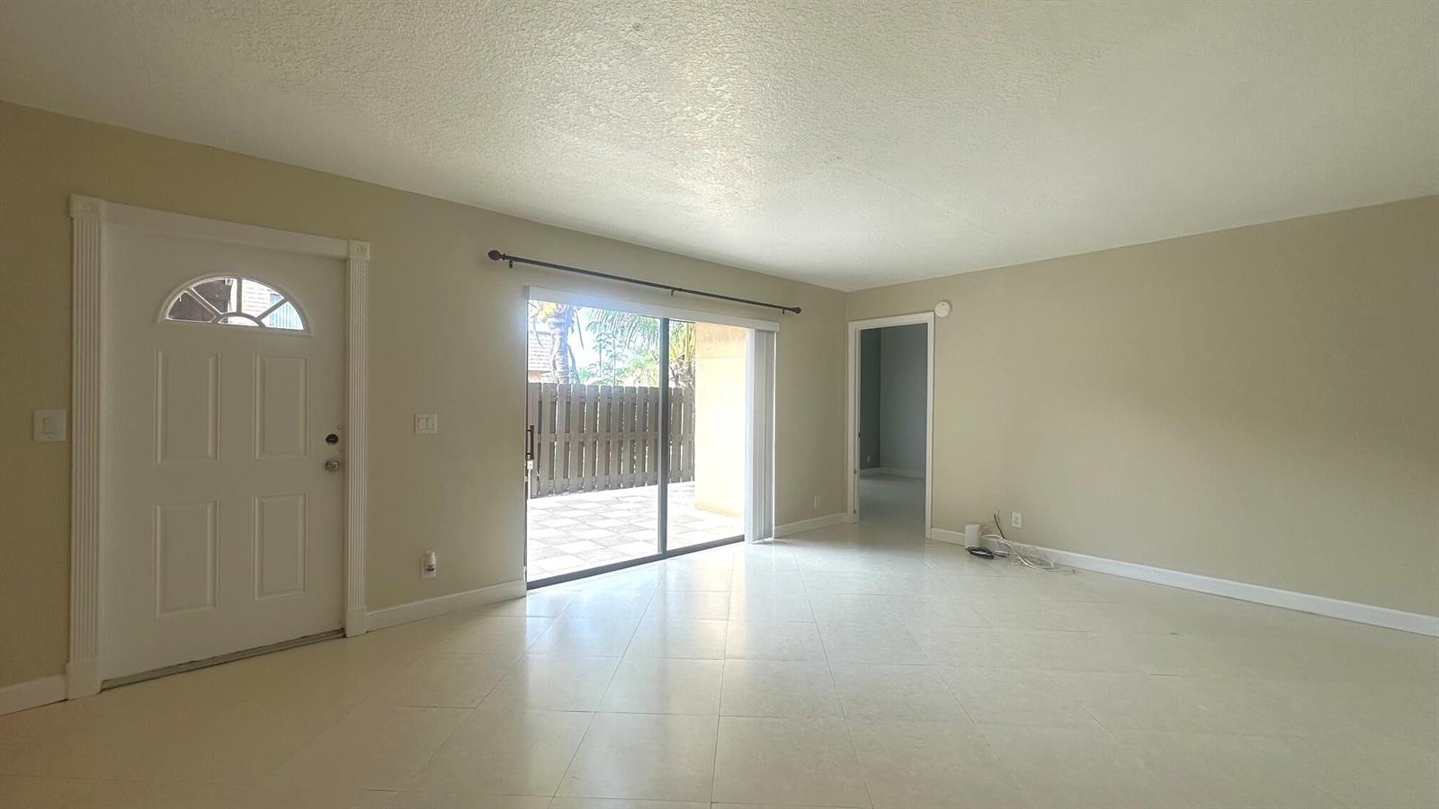 An empty living room features beige walls, tile flooring, a front door, and sliding glass doors — 303 Waterview Drive, Palm Springs FL 33461, PALM SPRINGS, FL