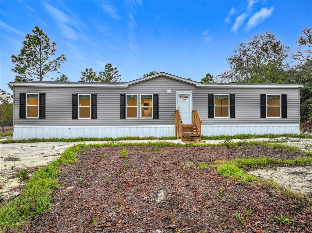 A single-story manufactured home with gray siding and a white front door sits outdoors — 150 LAKE GALILEE DRIVE, HAWTHORNE, FL