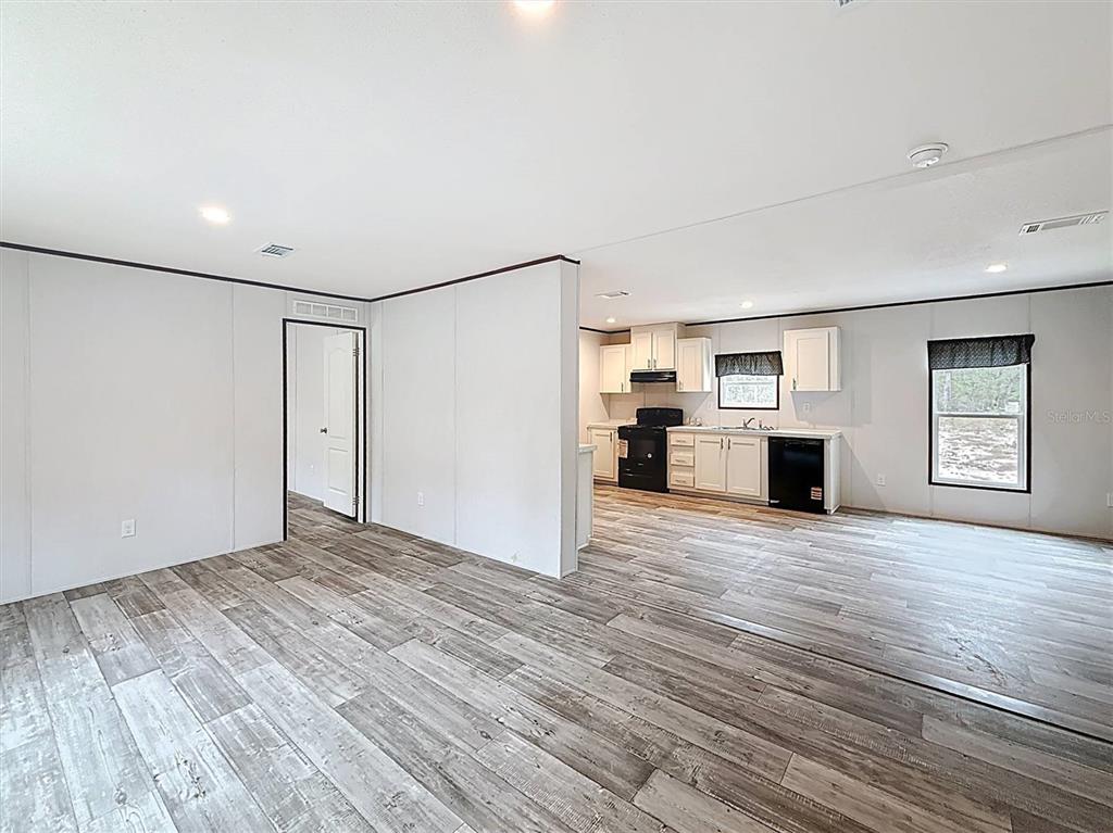 A living area with wood-look flooring opens into a kitchen featuring white cabinets and appliances — 150 LAKE GALILEE DRIVE, HAWTHORNE, FL