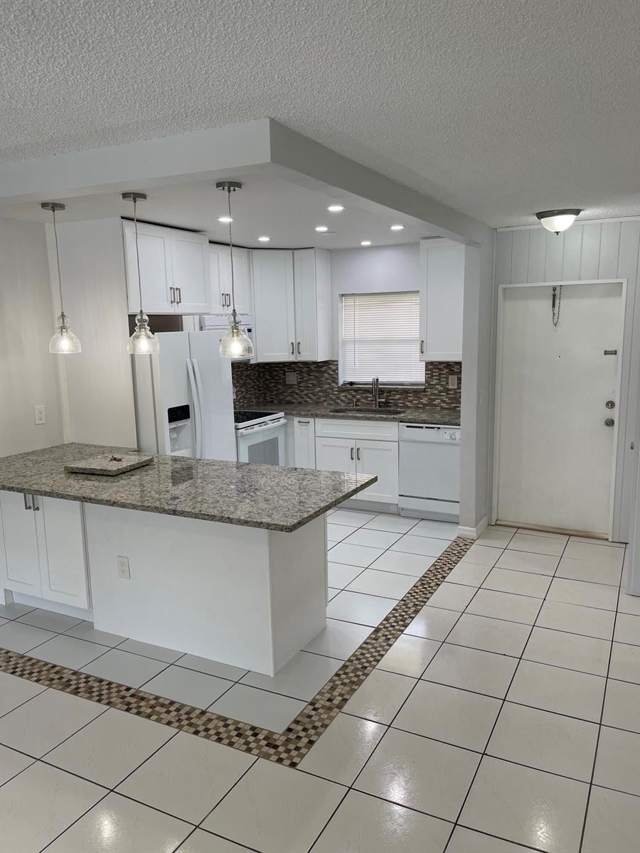 A kitchen with white cabinets, granite countertops, a breakfast island, and tiled flooring — 440 SE 2nd Avenue # 5, Deerfield Beach FL 33441, DEERFIELD BEACH, FL