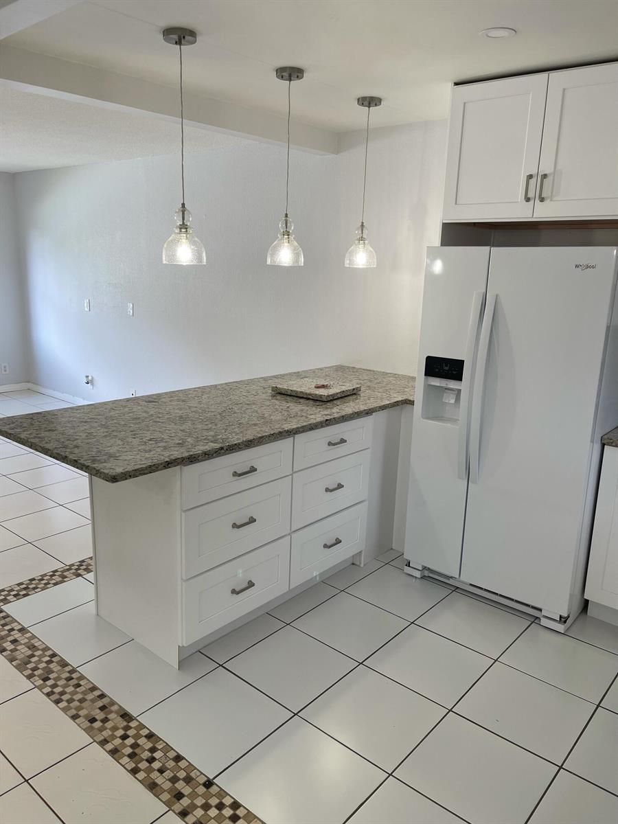 A kitchen island with granite countertops and white drawers sits beside a white refrigerator — 440 SE 2nd Avenue # 5, Deerfield Beach FL 33441, DEERFIELD BEACH, FL