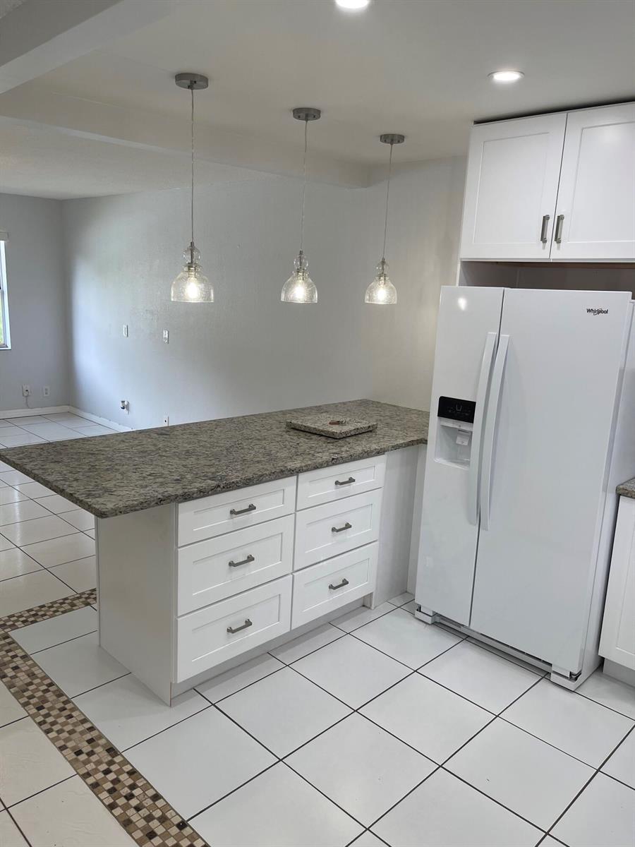 A kitchen island with granite countertops and white cabinets sits next to a white refrigerator — 440 SE 2nd Avenue # 5, Deerfield Beach FL 33441, DEERFIELD BEACH, FL